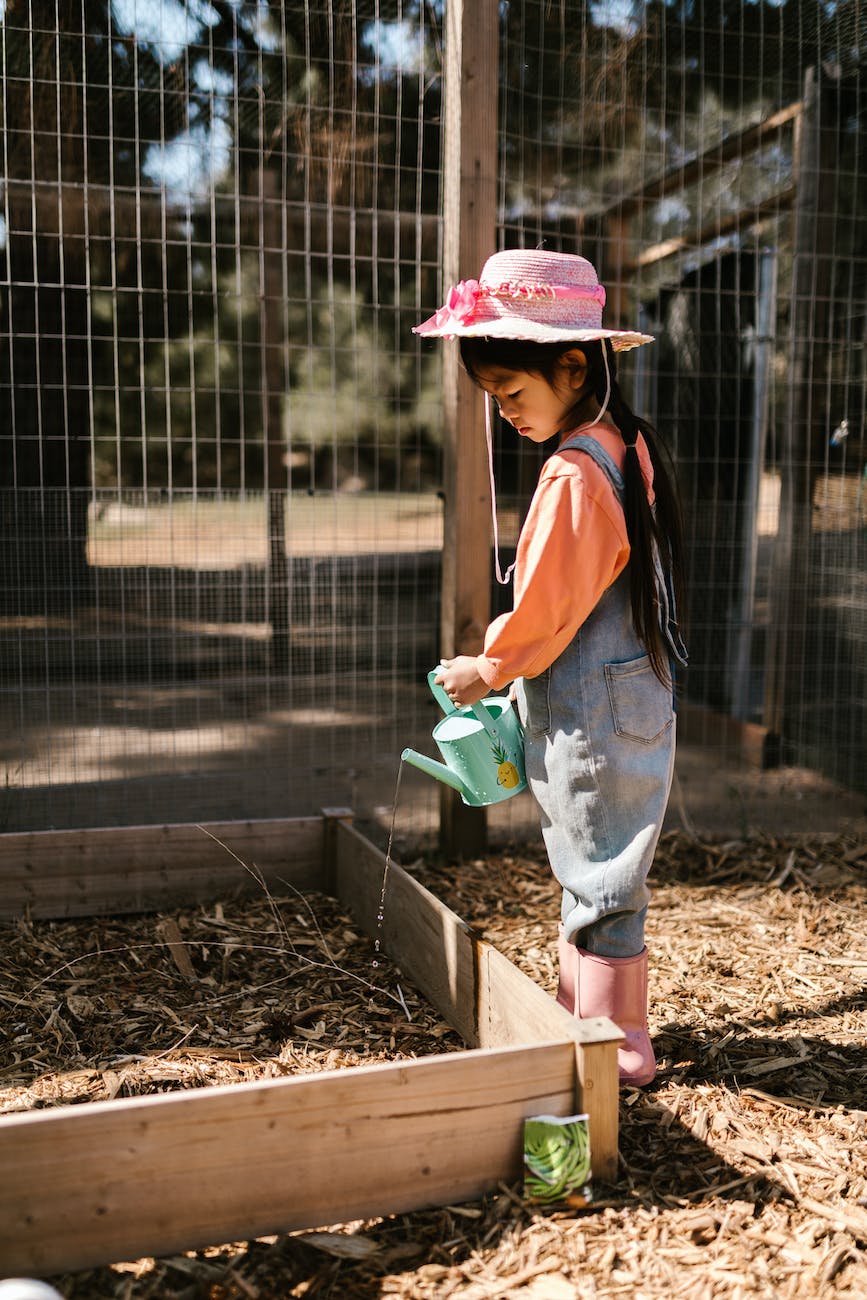 girl in overall and hat watering garden